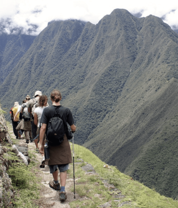 Viajeros caminando el Camino Inca hacia Machu Picchu durante trekking en los Andes
