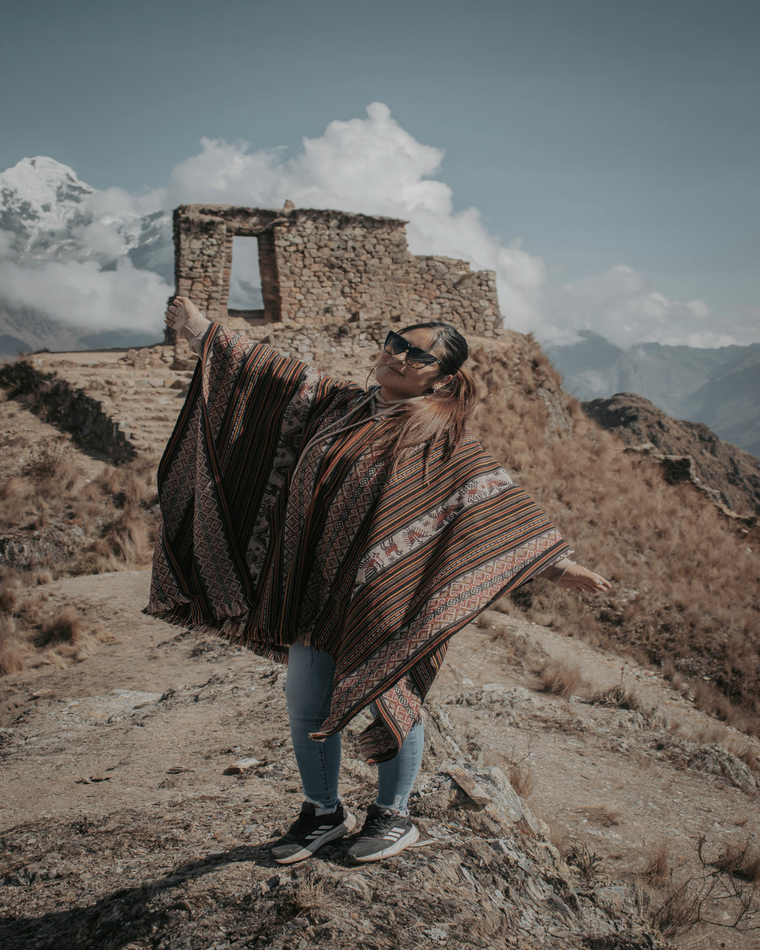 Mujer con poncho peruano frente a montañas en el Valle Sagrado de los Incas