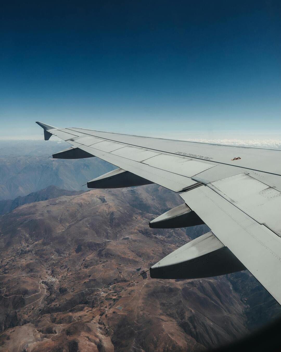 Avion-Peru-montanas Vista desde el ala de un avión sobrevolando los Andes en la región de Cusco, con montañas andinas extendiéndose bajo las nubes.