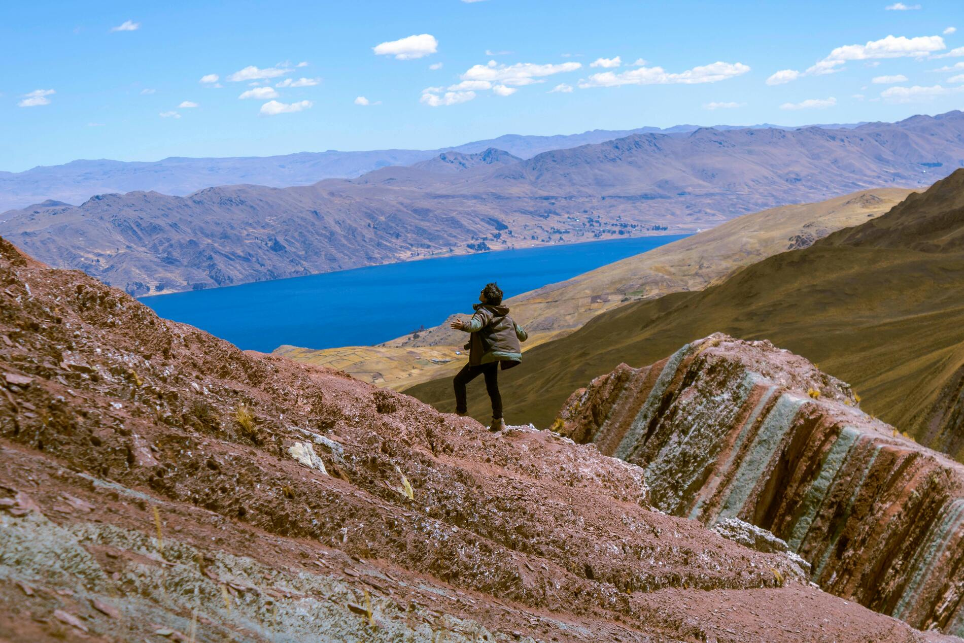 Hombre con los brazos extendidos disfrutando de la tranquilidad y de la impresionante vista de la laguna en Pallay Punchu, Cusco