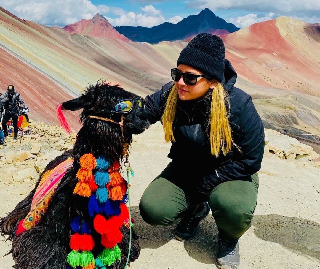 Mujer junto a una llama con gafas de sol en Vinicunca, la famosa Montaña de Colores de Cusco.