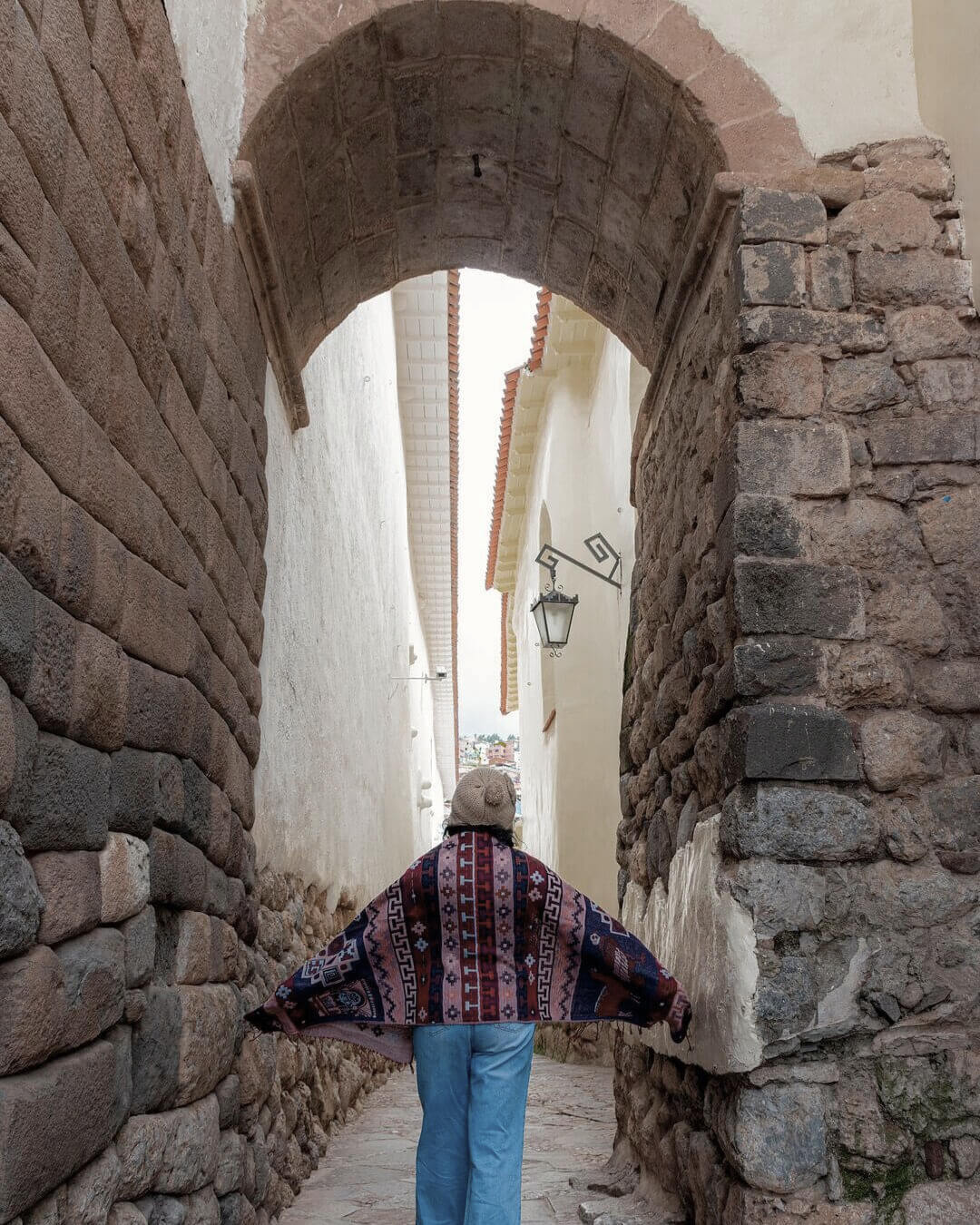 Mujer con poncho caminando bajo un arco colonial en el centro histórico de Cusco