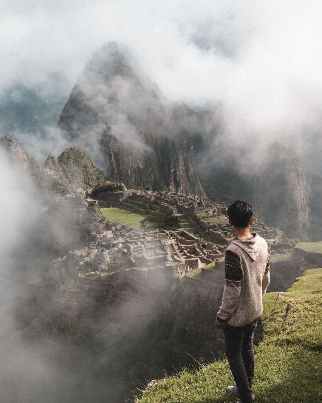 Hombre mirando Machu Picchu con neblina durante la mañana